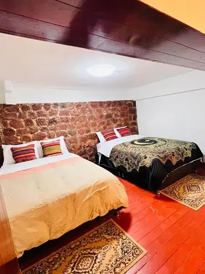 a bedroom with two beds and a brick wall at SkyGuest Cusco San Cristobal in Cusco