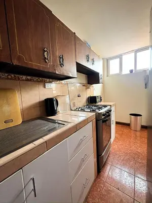 a kitchen with wooden cabinets and a stove top oven at Miraflores, habitación Triple en apartamento compartido in Lima