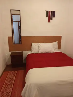 a bedroom with a bed with a red blanket and a mirror at Yuraq Wasicha in Cusco