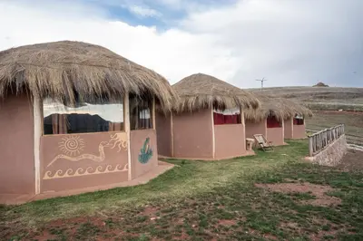 a row of huts with thatched roofs in a field at Pachamama Hampina Wasi Ancestral Center in Urubamba