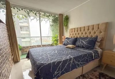 a bedroom with a bed with a blue comforter and a window at Dpto exclusivo en San Miguel con piscina y gym in Lima