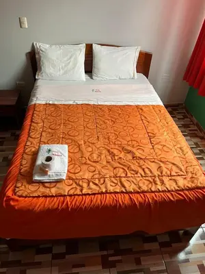 a bed with an orange comforter and a book on it at Hotel PRADO'S in Satipo