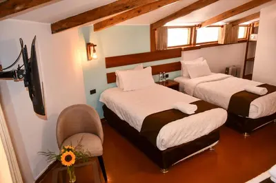 two beds in a room with a chair and a tv at Hotel Boutique MIRANDO AL SOL in Ollantaytambo