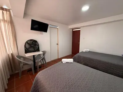 a hotel room with two beds and a desk and a television at Hostal La Reserva - Pisco in Pisco