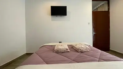a bed with a purple blanket and a tv on a wall at Casa Departamento en el Valle de Urubamba in Urubamba