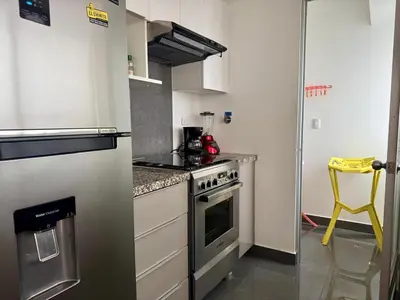 a small kitchen with a stove and a yellow stool at Departamento completo vista al mar,piscina,gimnasio,WIFI,Tvs in Lima