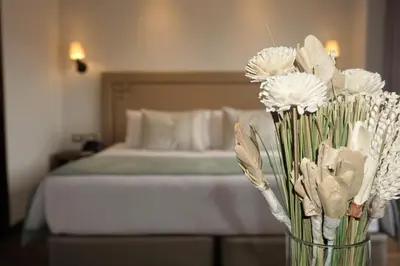 a vase filled with white flowers in front of a bed at Casa Esmeralda by Katari in Cusco