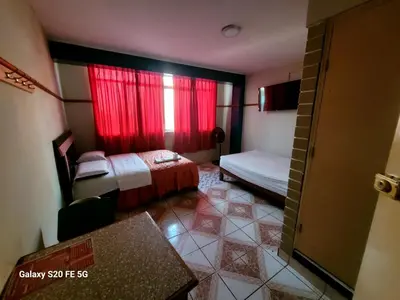 a small room with a bed and a red window at Las Estrellas Hostal in Puente Piedra