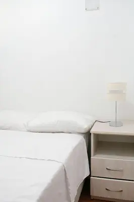 a white bedroom with a bed and a nightstand with a lamp at Apart Hotel Alojate Kaypi in Ayacucho