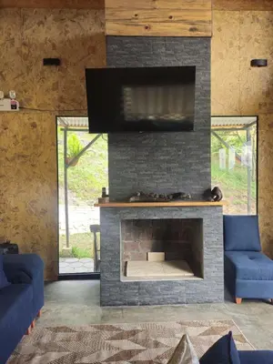 a living room with a stone fireplace with a flat screen tv at La Montaña Lodge - Oxapampa in Oxapampa