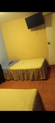a room with two beds and a tv on the wall at Hospedaje Puerto Escondido in Pucusana