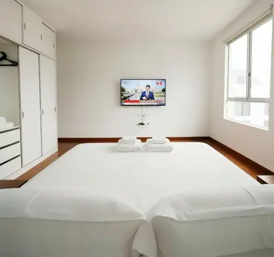 a white bedroom with a white bed and a tv on the wall at E Suite Tourist free Parking Miraflores 1B 503 in Lima