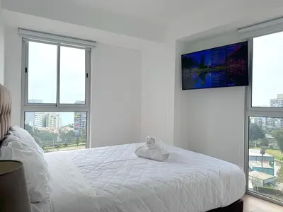 a white bedroom with a bed with a tv on the wall at Peruvian Apartments Barranco 1404 in Lima