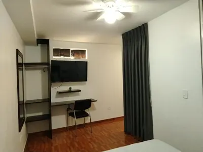 a room with a bed and a television and a chair at Hostal Mirador in Pisco