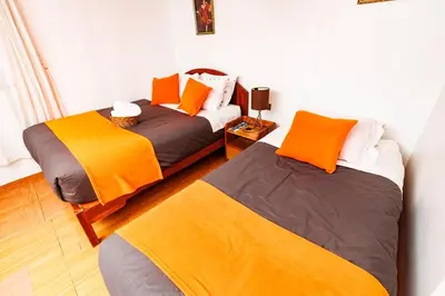 two beds in a room with orange and gray at Mayu House Inn a minutos del centro histórico in Cusco
