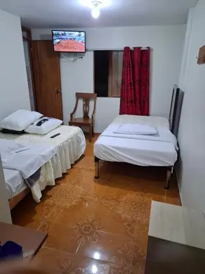 two beds in a room with a tv on the wall at Hospedaje Las Brisas in Churín