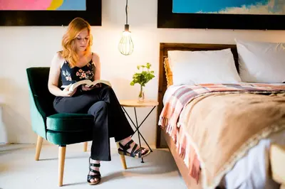 a woman sitting in a chair reading a book in a bedroom at Niños Hotel Meloc in Cusco