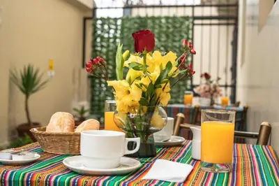 a table with a vase of flowers and orange juice at Hotel Manhattan Inn Airport in Lima