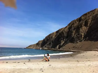 a woman sitting on a beach next to the ocean at Paracas vista al mar in Paracas
