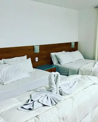 two beds with white sheets and a towel on them at Hotel Balistra in Ica