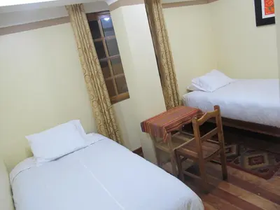 a room with two beds and a chair and a window at Tumy house B&B in Ollantaytambo