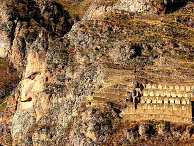 a rock cliff with a building on the side of it at Hospedaje K'uchuwasi in Ollantaytambo