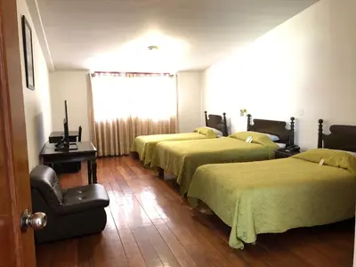 a room with four beds and a chair and a window at Hotel de Turistas Abancay in Abancay