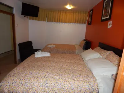 a hotel room with two beds and a chair at Hospedaje Qori Punku in Cusco