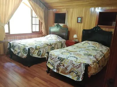 two beds in a room with wooden walls and wooden floors at Illariy Tampu Ecoalbergue Oxapampa in Oxapampa