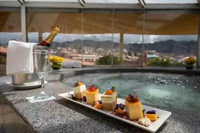 a plate of food and a bottle of wine next to a pool at Hotel Jose Antonio Cusco in Cusco
