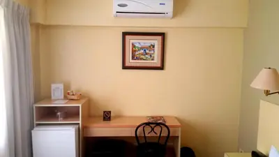a room with a desk with a refrigerator and a fan at Embajadores Hotel in Lima