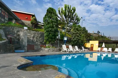a swimming pool with chairs and trees and a building at Decameron El Pueblo in Lima
