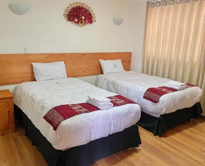 two beds in a hotel room with white sheets at Hostal Casona Arrambide in Cusco