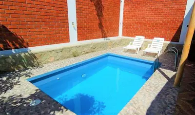 a swimming pool with two chairs next to a brick building at Casa de Campo Belén - Lunahuaná in Lunahuaná