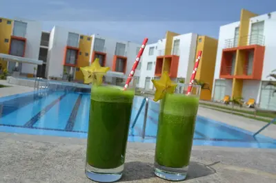 two green drinks with straws sitting next to a pool at Kajaca Suite Hotel in Huacho