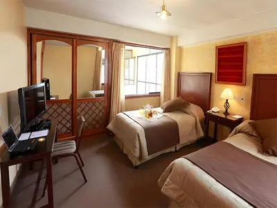 a hotel room with two beds and a desk and a television at Hotel El Puma in Cusco