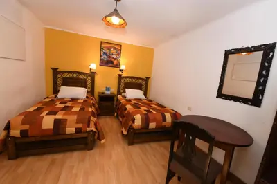 a room with two beds and a table and a mirror at Departamentos Cusco in Cusco