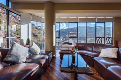 a living room with leather furniture and large windows at Espacioso confortable apartamento familia in Cusco