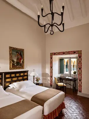a bedroom with two beds and a table and a chandelier at Monasterio, A Belmond Hotel, Cusco in Cusco