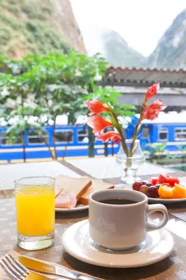 a table with a cup of orange juice and a plate of fruit at Inti Punku Machupicchu Hotel & Suites in Machu Picchu