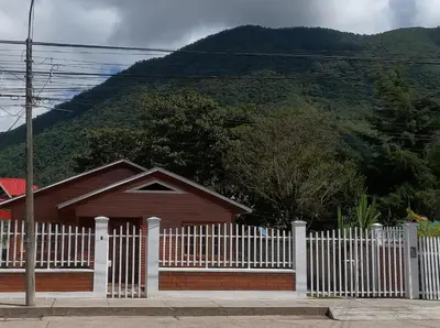 a house with a white fence in front of a mountain at Cabañas Típicas ARIAS in Oxapampa