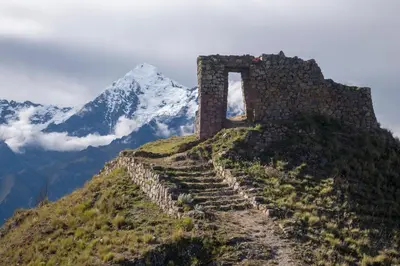 a stone building on a hill with a mountain in the background at SAUCE Hotel Boutique in Ollantaytambo