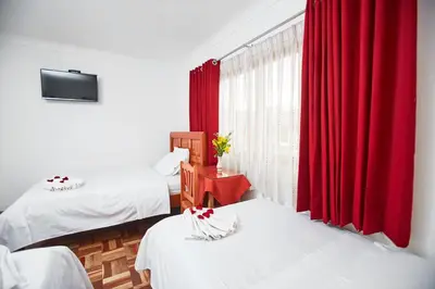a room with two beds and a window with red curtains at Hostal Danna Inn in Cusco