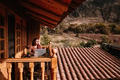 a woman sitting at a table with a laptop on a porch at Inkasaire Boutique Lodge in Urubamba