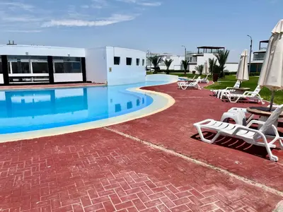 a swimming pool with chairs and umbrellas next to a building at Duplex 1 Fila Vista Bahía Paracas - Sotavento 501 T3 in Paracas