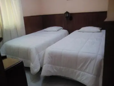 two beds in a hotel room with white sheets at Hotel Princess in Ica