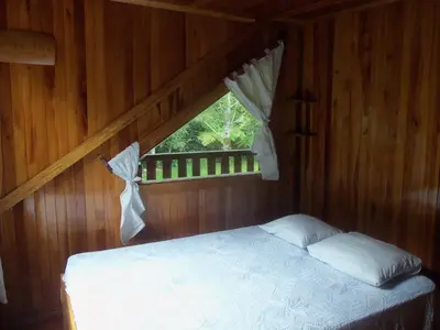 a bed in a wooden room with a window at Refugio de Orquídeas in Oxapampa