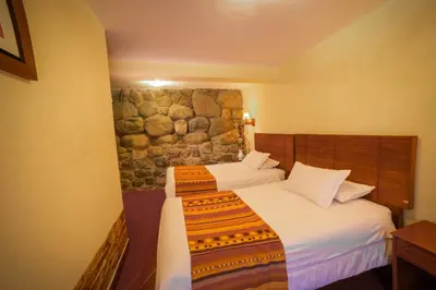 a bedroom with two beds and a stone wall at Siete Ventanas in Cusco