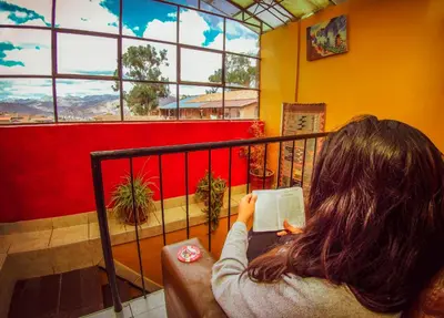 a woman sitting on a balcony reading a book at Flying Dog Hostel Cusco in Cusco