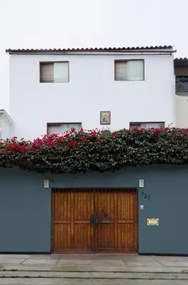a white building with a wooden door and red flowers at Jose Luis Hostal Boutique in Lima
